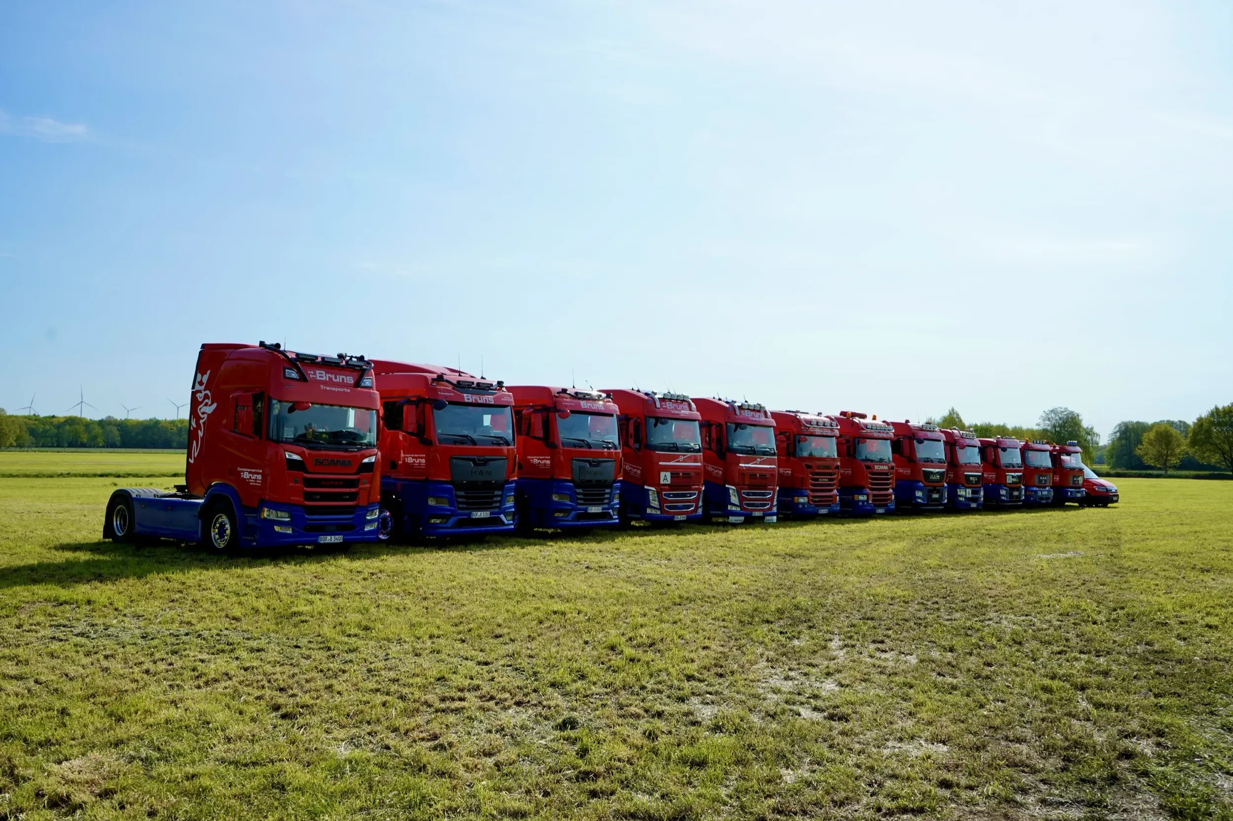 Die Sattelzugmaschinen von Bruns Transporte in einer Reihe auf der Wiese